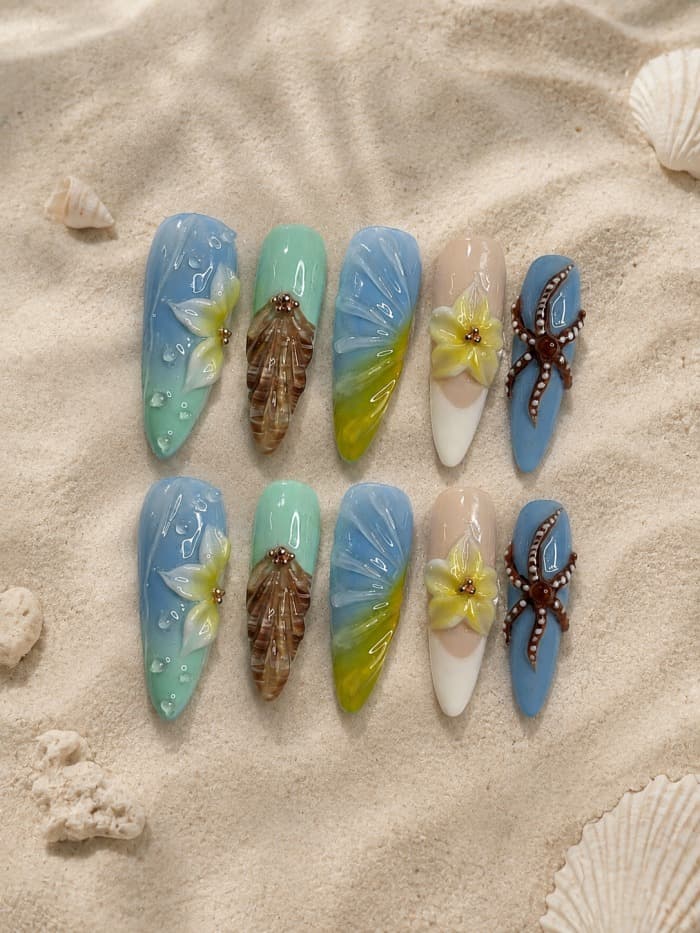 Beachside Bliss — Ocean-blue nails with water-droplet texture, a 3D shell charm, a hibiscus flower and a starfish charm, shot on real sand