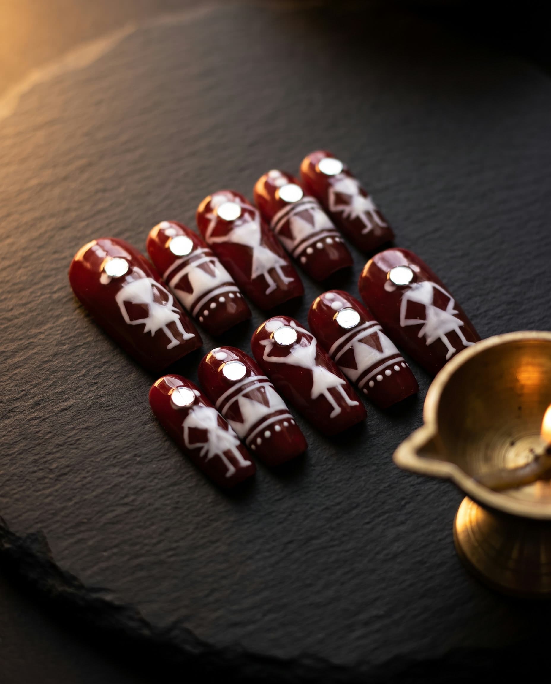 Warli Tales — Hand-painted Warli folk dancers on deep maroon, styled with brass and firelight